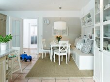 A white living room-cum-kitchen with a comfortable bench, a cabinet and a tiled floor