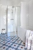 Bathtub, glazed shower cabinet, white-tiled walls and cement floor tiles with floral pattern in bathroom