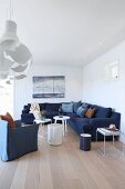Living room with white wood cladding, dark blue corner couch and armchair around white side tables