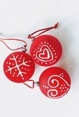 Red Christmas-tree baubles with hand-painted motifs on white surface