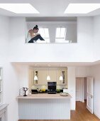 Blick auf Einbauküche mit Küchentheke unter modernem Galerieausschnitt mit Glasbrüstung und Oberlichtfenster
