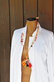 Verschiedene gehäkelte Schnüre mit Holzperlen und Bommel als Halskette an Schneiderpuppe mit weißer Bluse