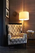 Comfortable reading chair next to lit standard lamp and brass side table