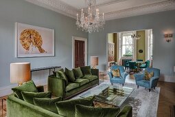 Elegante Sofagarnitur aus grünem Samtstoff und hellblaue Sessel in herrschaftlichem Wohnzimmer, an Stuckdecke mehrarmiger Kronleuchter