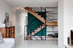 Blick vom Wohnraum in offenes Treppenhaus auf schwarzes Metallgeländer vor edler Holztreppe
