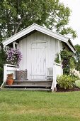 Weisses Gartenhäuschen aus Holz mit kleiner Veranda und Blumenampel