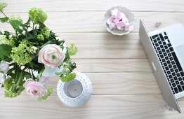 Laptop, white tealight holder and romantic bouquet arranged on solid wooden table top