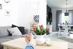 Woman's feet propped next to vase of red tulips on wooden couch table