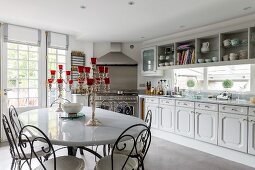 Metal dining chairs around silver candelabras on white table in front of country-house kitchen counter