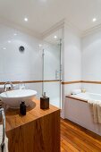 Exotic-wood washstand with white countertop basin opposite bathtub and shower