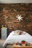 Jungenzimmer mit Bett vor rustikaler Ziegelwand, weiße Sternleuchte an Wand