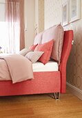 A salmon-coloured box spring bed with an upholstered frame and cushions
