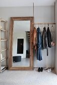 Minimalist coat rack suspended from ceiling on leather straps and hooks next to rustic full-length mirror