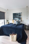 Double bed with dark blue bedspread flanked by minimalist pendant lamps