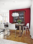 White, leather-covered bucket chairs around an oak dining table opposite a buffet against a Bordeaux red wall