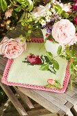 Romantischer Gartenblumenstrauss in Porzellankanne auf gestricktem Deckchen mit Rosenmotiv