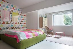 Helles Schlafzimmer mit bunter Tapetenwand und grün gepolstertem Bettgestell