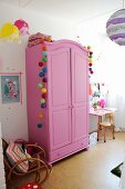 Pinkfarbener Kleiderschrank mit bunten Kugelgirlanden dekoriert in Mädchenzimmer