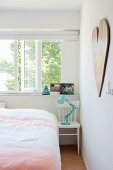 Turquoise retro lamp on white wooden chair used as bedside table below open window