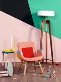 Collection of stools and armchair next to standard lamp against wall with geometric pattern of bright colours