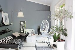 Couch, hanging chair, wall lamp and plants in modern living room in shades of grey