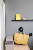 Narrow black floating shelf above yellow bag hung from black peg on grey wall