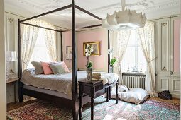 Bed with wooden frame in romantic bedroom with pastel pink walls annd floral home textiles