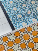 Verschiedene Bodenbeläge: weisser Dielenboden, blau-weiße Ornamentfliesen und ockerfarbene Fliesen mit geometrischem Muster