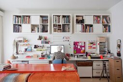 Woman sitting at long desk below high shelves in home workspace