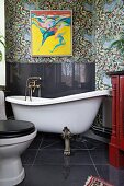 Vintage Badezimmer mit freistehender Badewanne auf Löwenfüssen, schwarz gefliester Spritzschutz an Wand, oberhalb modernes Bild auf floraler Tapete
