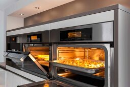 An illuminated oven and a combi-steamer with an open door at eye level