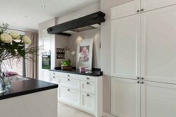 An open-plan kitchen with a white, built-in cupboard next to a work surface in a niche with an integrated extractor fan