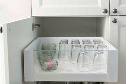 An open kitchen cupboard with glasses in a drawer