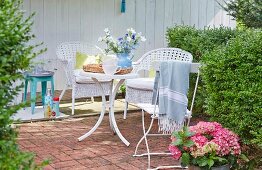 A terrace with white wicker chairs, a folding chair and table in a summery garden