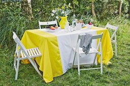 Selbst genähte gelb-weiße Tischdecke auf sommerlichen Tisch im Freien