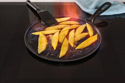 Pans with flambéed mango pieces on an induction stove