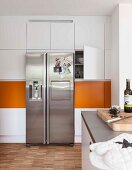 Built-in cupboards with orange panels and a stainless steel fridge-freezer combination