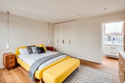 Schlafzimmer mit gelbem Bett, Einbauschrank und Bad