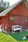 White garden bench below hanging basket outside Falu-red barn