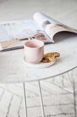 Mug and biscuit on saucer and magazine on white tray table
