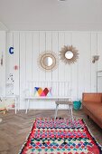 Round mirrors on white wooden wall, wooden bench and colourful rug in living area