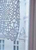 A transparent sticky hook on a window to hold a crocheted curtain