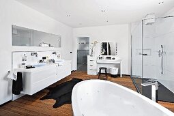 A bright white bathroom with a wooden floor, make-up table and shower area with glass panels