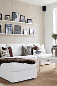White sofa, accessories in earthy tones and pictures on narrow shelves on beige wall