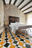 Double bed with antique headboard against traditional stone wall on multicoloured geometric tiled floor