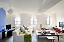 Pale sofa, coffee table, designer chairs and low sideboard in lounge area with arched windows, blue partition and designer table