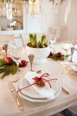 Zapfen mit roter Kordel um weißes Gedeck auf weihnachtlich geschmücktem Esstisch