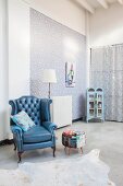 Antique blue leather armchair and vintage display cabinet on concrete floor in loft apartment with floral wallpaper