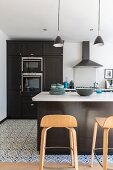 Black fitted kitchen with white worksurface and designer bar stools