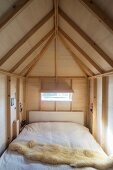 Bett mit Schaffell in holzverkleideten Raum mit Dachbalkenkonstruktion